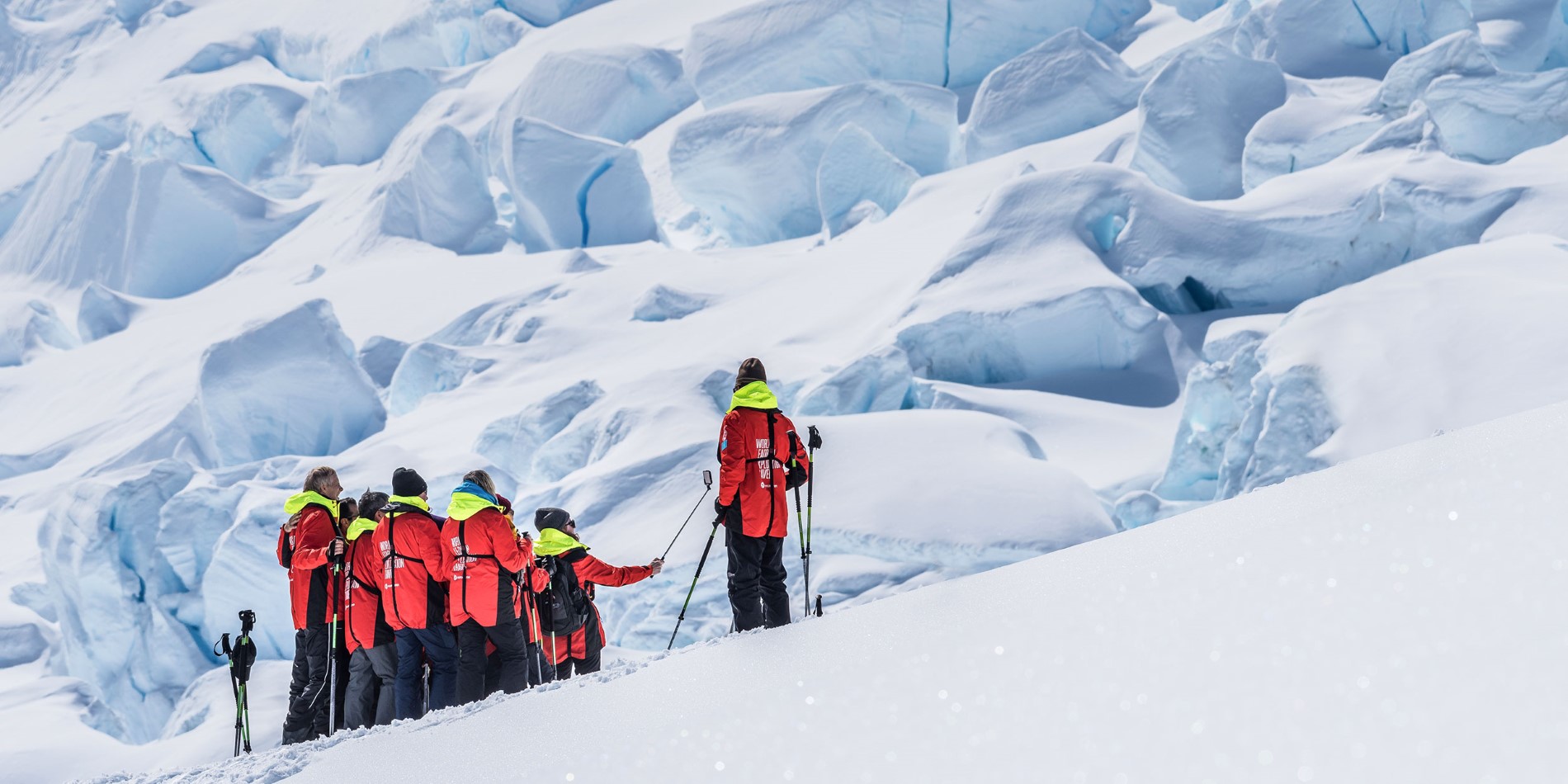 People in red expedition jackets hiking up an iceberg.