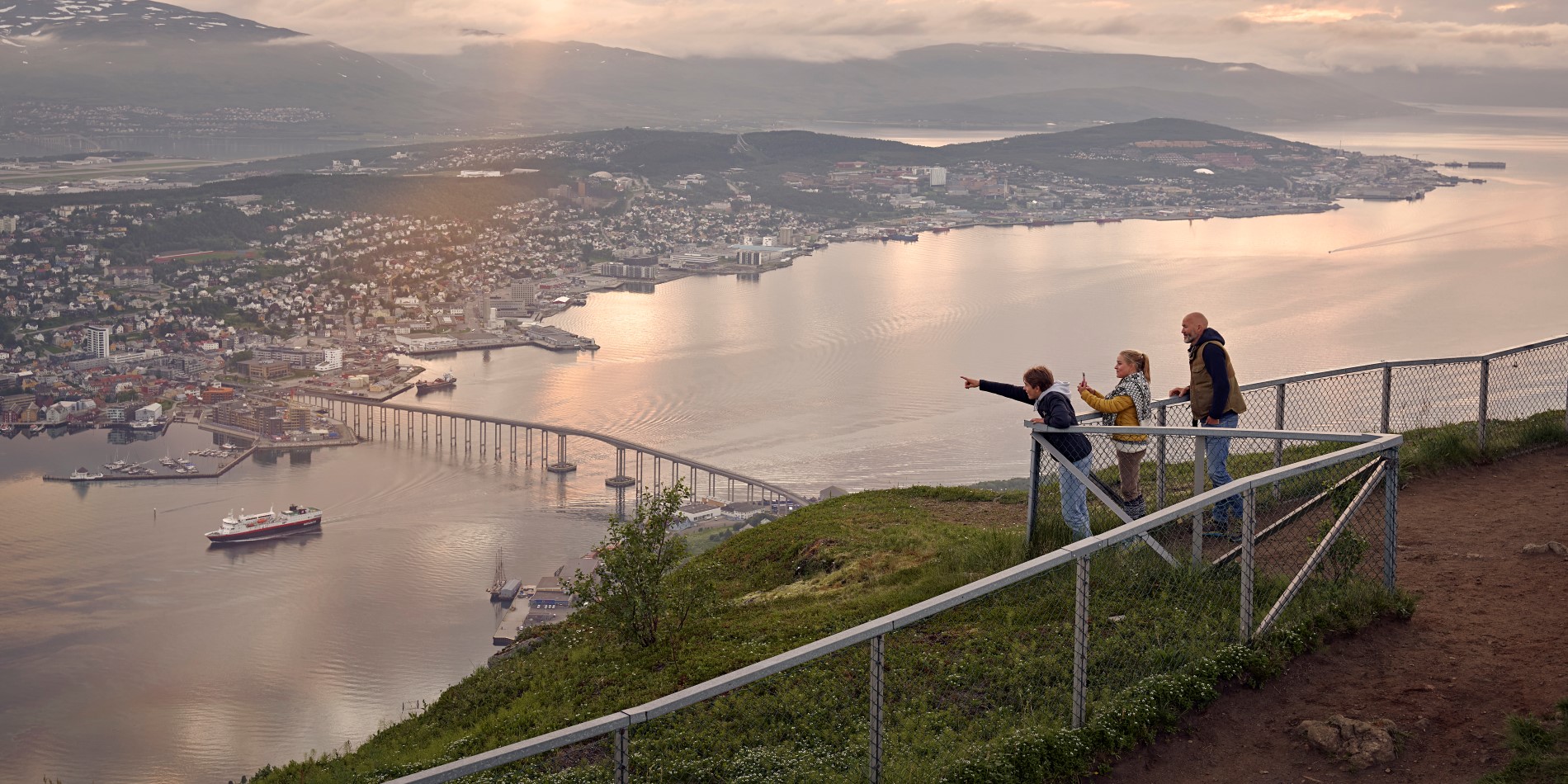 Drei Kinder stehen hinter dem Zaun auf dem Stadtberg in Tromsø. Sie blicken auf die Stadt Tromsø herab.